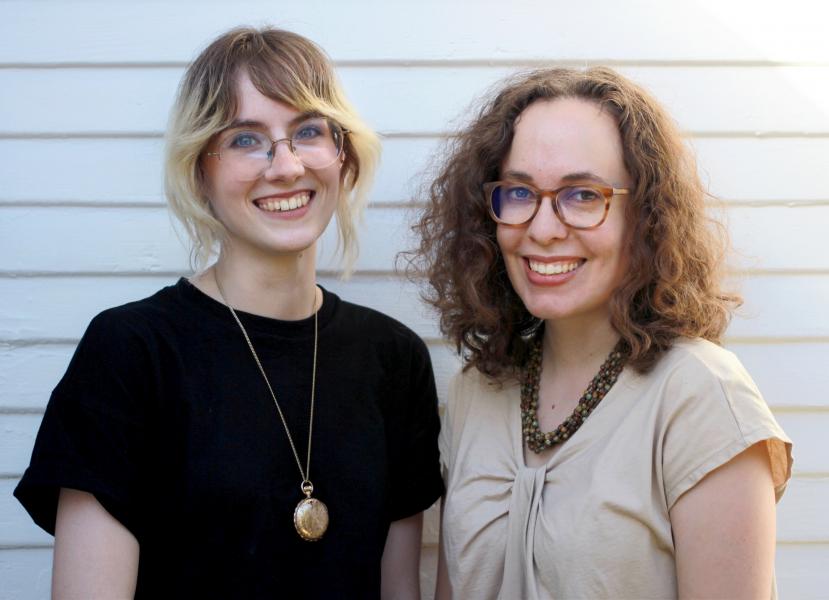 Meghan Boehman and Rachael Briner author photo. Two white women standing next to each other. Meghan on the left has brown and blond hair framing her face and glasses wearing a black shirt and a pendant necklace. Rachel on the right has curly short brown hair and tortoise shell glasses. She is wearing a light tan blouse with a beaded necklace.