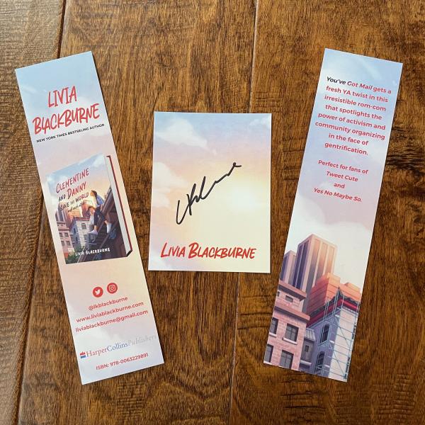 A photo of Clementine and Danny swag. A signed bookplate is in the center with a cloudy sky background. The left side shows one side of the bookmark with the cover of the book and the right side shows the some text and some buildings from the book's cover.
