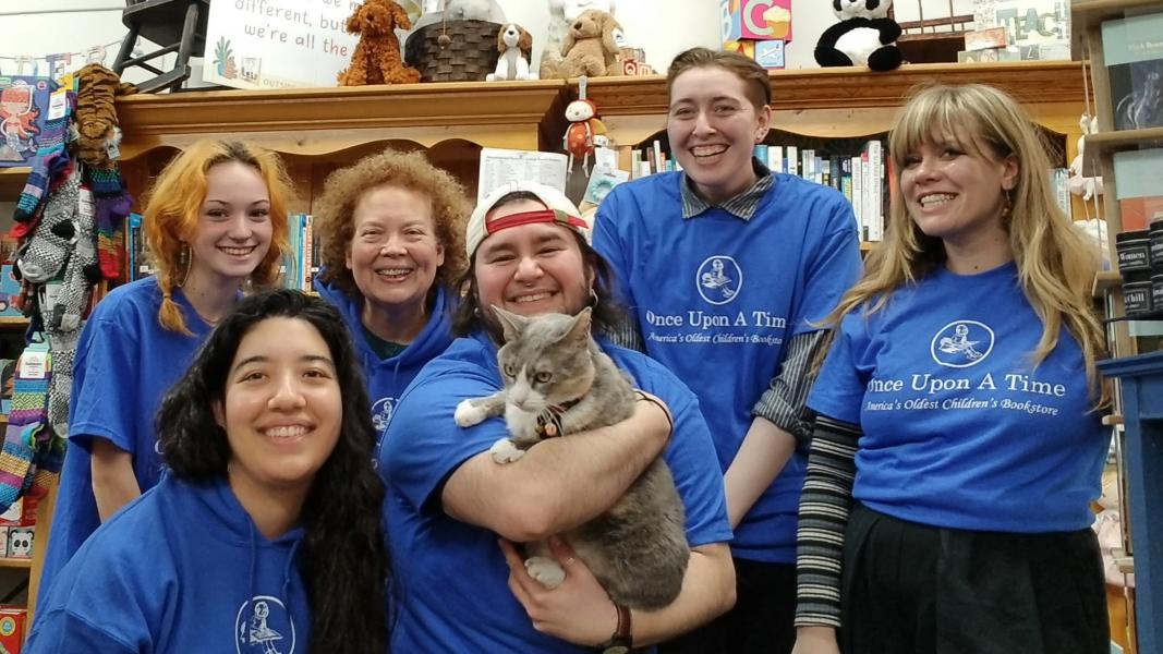 Once Upon A Time Staff from left to right Maddie, Jessica, Maureen, Apollo holding Pippi, Iz, and Maddi and in front of some bookshelves in the store.